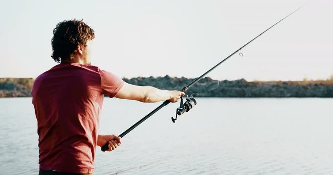 Young man fishing on a lake at sunset and enjoying hobby