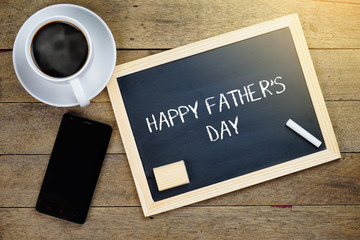 Top view of smartphone, hot coffee and chalkboard written with Happy Father's Day on wooden background.