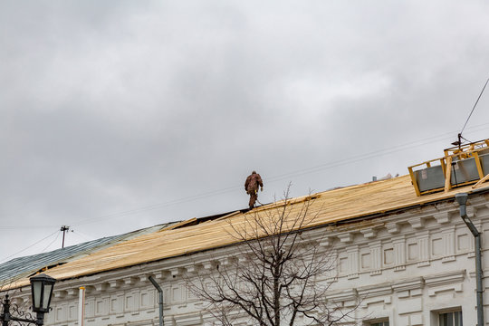 A man on the roof is carrying out repairs with wooden boards
