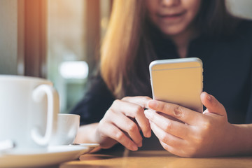 A beautiful Asian woman with smiley face holding and using smart phone with coffee cup on wooden table in the cafe