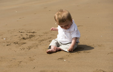 One year old baby boy playing with sand on the beach 