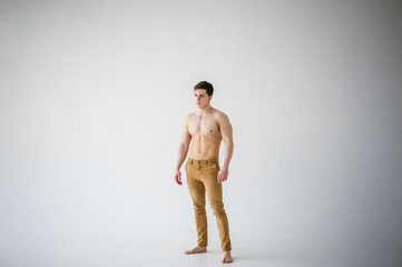 portrait young sexy handsome man of strong Athlete's body with bare torso, Dressed  brown trousers, Posing on white studio background