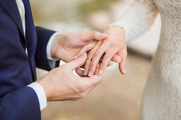 Obraz na płótnie Canvas White bridal couple at wedding ceremony outdoors. Closeup of young happy beautiful bride and handsome groom holding hands and exchanging golden rings. Horizontal color picture.