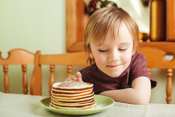 Cute little boy eating a stack of pancakes in the kitchen.