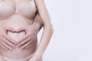 Couple forming heart out of her hands on Pregnant womans baby bump.copy space