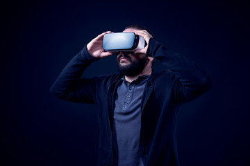 Young hipster bearded man wearing virtual reality goggles. Black background studio VR concept.