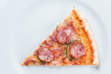 Delicious slice of pizza with sausages and pickles on a plate