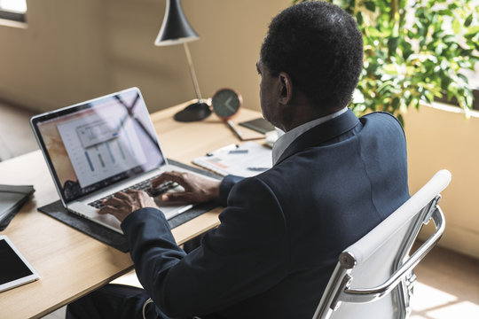 Middle-aged African businessman sitting at office and typing on his laptop.