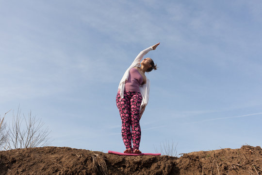 Young Woman Performing Yoga Side Stretch While Standing On Pile Of Soil