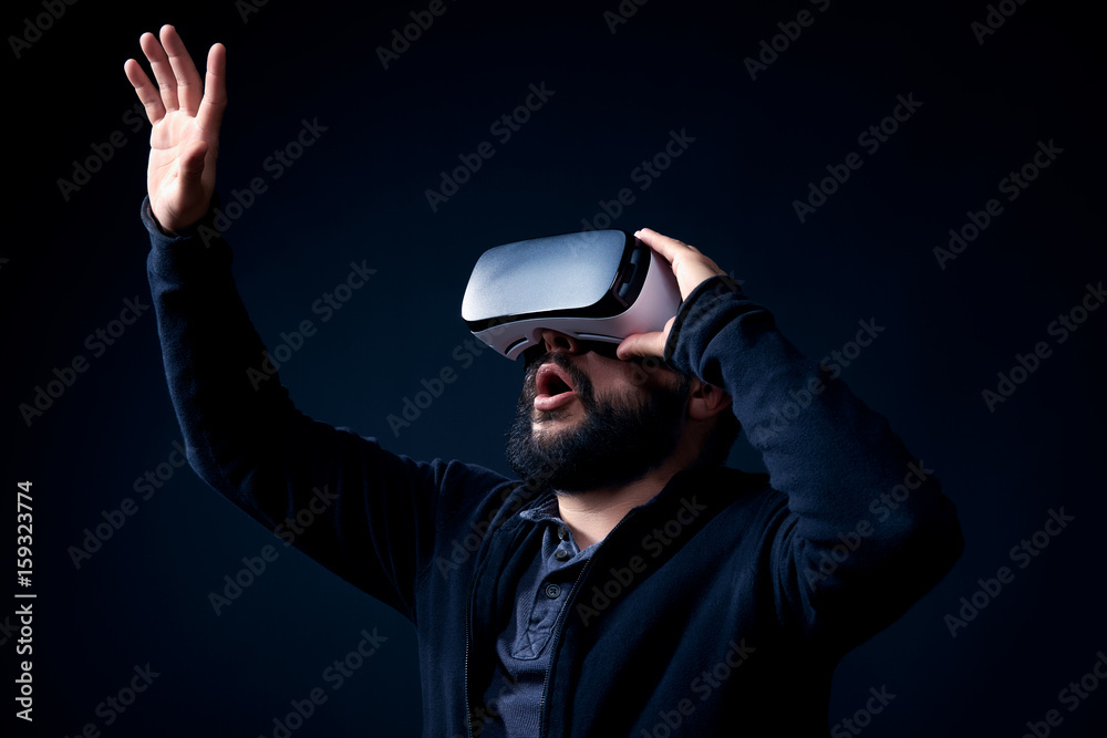 Wall mural young hipster bearded man wearing virtual reality goggles. black background studio vr concept.