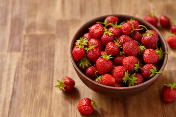 Fresh red strawberries in a brown clay bowl on wooden table.