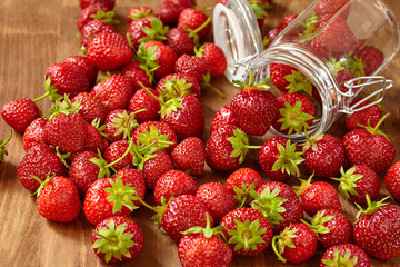 Fresh red strawberries for jam in a glass jar on the brown wooden table.