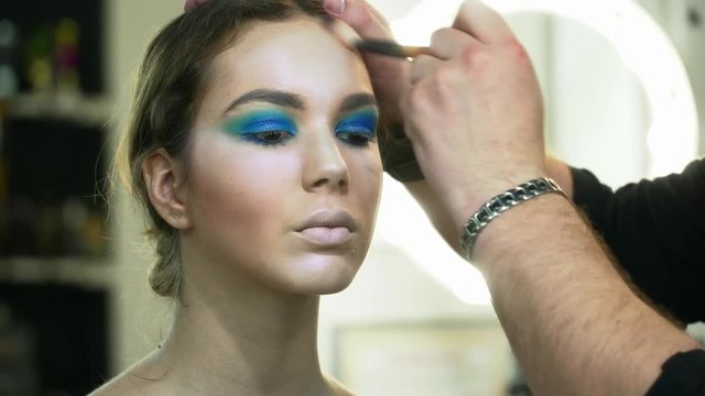 Makeup artist making beautiful face art for a young brunette woman with makeup brush