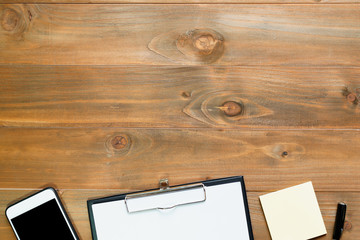 Top view of blank paper on wooden desk with smartphone, pen and  sticky note.