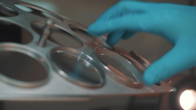 Scientist hand in blue rubber glove puts magnifier in hole of metal rotating device at manufacture, close up