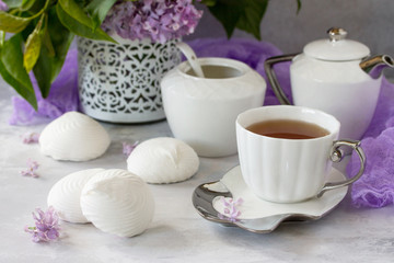Delicate vanilla marshmallow on a white delicate plate. Still life with marshmallows, a cup of tea and lilac lilac on a background of ancient stone.