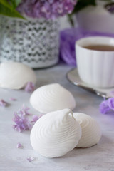 Delicate vanilla marshmallow on a white delicate plate. Still life with marshmallows, a cup of tea and lilac lilac on a background of ancient stone.