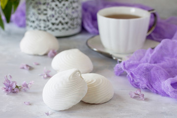 Fototapeta na wymiar Delicate vanilla marshmallow on a white delicate plate. Still life with marshmallows, a cup of tea and lilac lilac on a background of ancient stone.