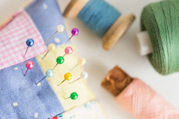 needlework, craft, sewing and tailoring concept - macro with beautiful stitched pincushion and colorful pins, pink, blue and green thread spools, white background, selective focus