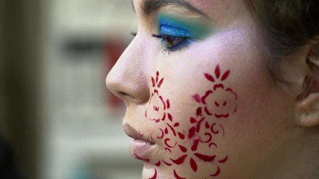 Makeup artist painting lips for a woman with face art