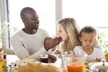 Young interracial family with little children having breakfast.