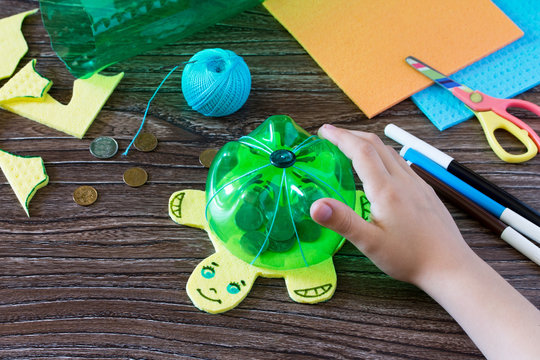 The child holds a children's hand-craft from a plastic bottle for money piggy bank. Handmade. Project of children's creativity, handicrafts, crafts for children.