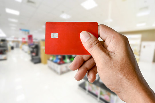 A Hand Holding Credit Card On Blurred Electronics Store