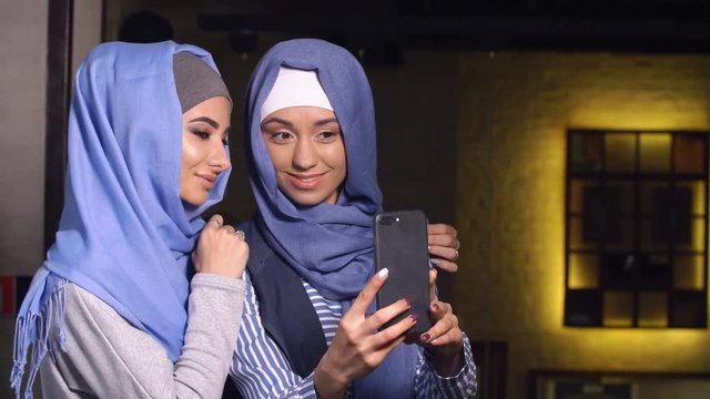 Modern Muslim women take pictures on a mobile phone. Girls in hijabs talking and smiling