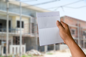 a hand holding saving account bank book on construction house