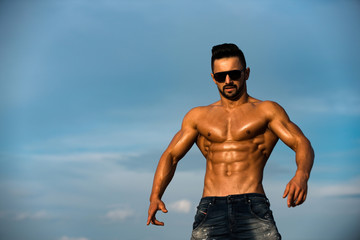 sexy man with muscular body in sunglasses on blue sky