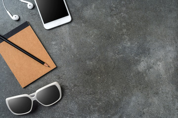 Obraz na płótnie Canvas White smartphone, earphones, sunglasses and notebook on gray stone background