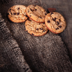 Obraz na płótnie Canvas Chocolate cookies on dark napkin on wooden table. Chocolate chip cookies on brown coffee color cloth, macro, top view