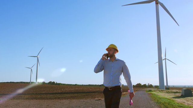 The engineer goes and talks on the phone against the background of windmills.