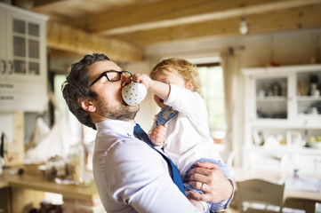 Businessman holding little son in the arms, drinking coffee.