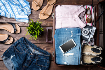 Open suitcase with casual female clothes on wooden table