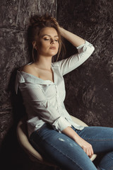 Glamorous young model sitting on a chair  in striped and torn jeans