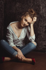 Fototapeta na wymiar Seductive young woman in shirt and jeans sitting on the floor