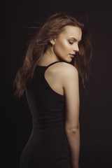 Naklejka premium Stylish brunette model in black dress with curly hair in motion