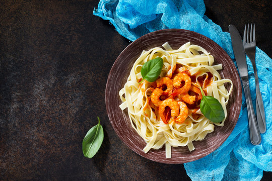 Spaghetti with tomato sauce and shrimps in a plate on dark concrete, stone or slate background.