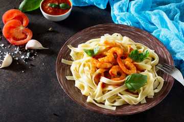 Spaghetti with tomato sauce and shrimps in a plate on dark concrete, stone or slate background.