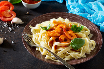 Spaghetti with tomato sauce and shrimps in a plate on dark concrete, stone or slate background.