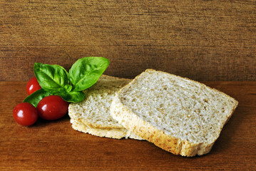 Two slices of toast, made from whole meal, on a wooden plate with a leaf of Basil and some little tomatoes