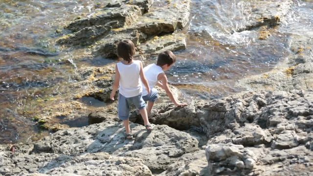 Two children, boys, running on rocks on the shore of the sea, having fun