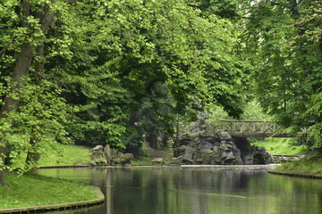 Fototapeta na wymiar L'étang principal en zigzag avec son pont rustique et ses faux rochers sous la nature luxuriante du parc Josaphat à Schaerbeek 