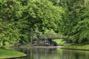 Fototapeta na wymiar Le pont rustique et ses faux rochers sous la nature luxuriante au printemps du parc Josaphat à Schaerbeek 