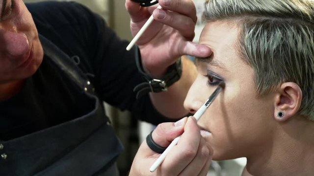 Male makeup artist making face art for a young blonde man