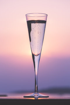 Glass of prosecco at a wooden pier at sunset. Luxury resort vacation concept. Festive relax getaway background.