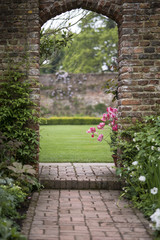 Old archway in old English country garden landcape in Spring with tulips and border plants