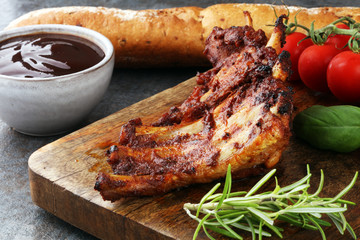 Spicy hot grilled spare ribs from a summer BBQ served with fresh tomatoes on an old vintage wooden cutting board