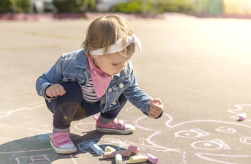 girl in a jeans jacket draws with colored chalks